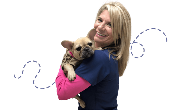 A smiling woman holding a small fawn-colored French Bulldog.