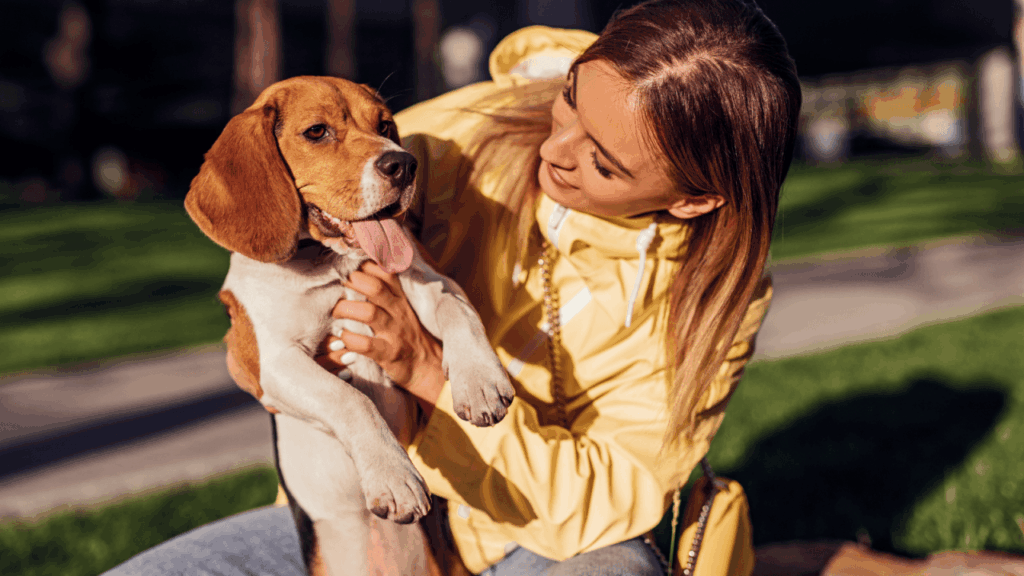 Young woman lovingly holding a beagle puppy in a sunny park.