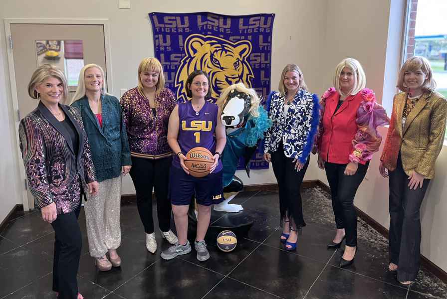Group of seven women posing with a costumed LSU mascot holding a basketball.
