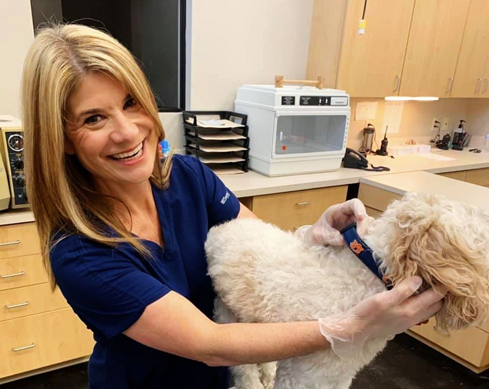 Woman in blue scrubs smiling while holding a fluffy white dog in a lab environment.