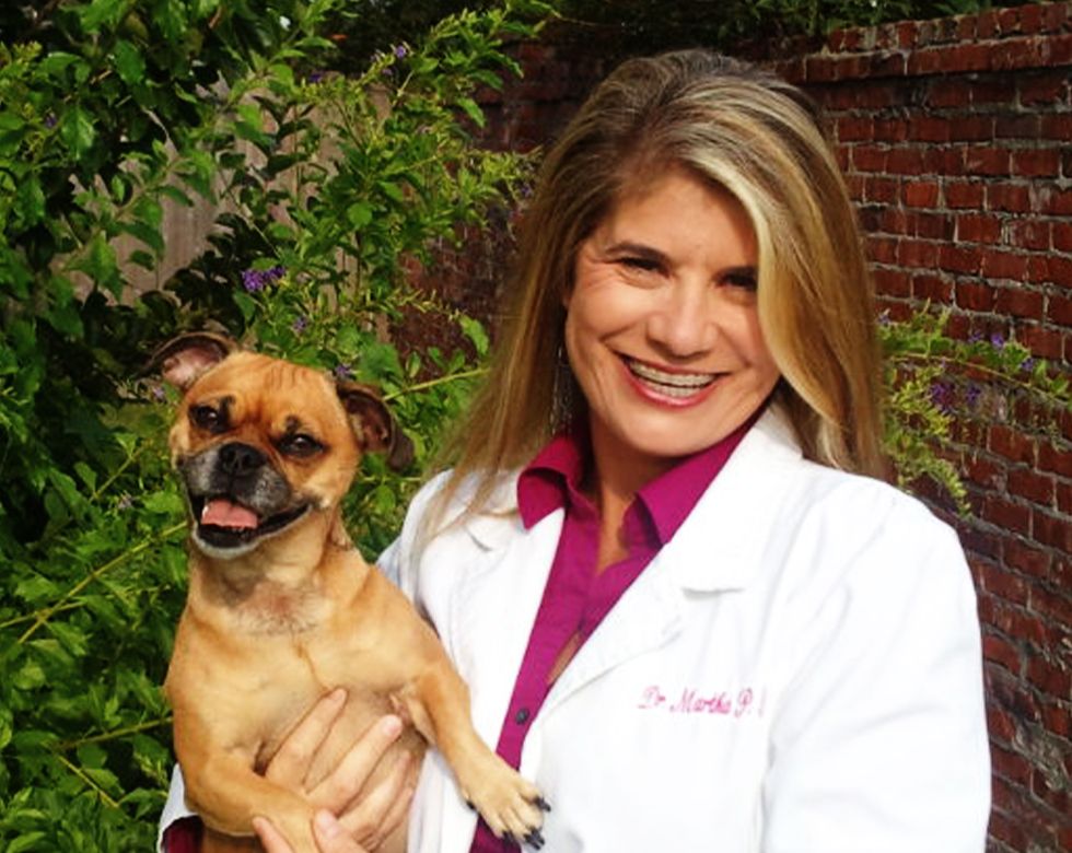 Smiling woman in a white coat holding a happy small dog.