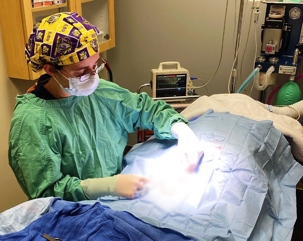 Surgeon in scrubs and mask performing a procedure in an operating room.