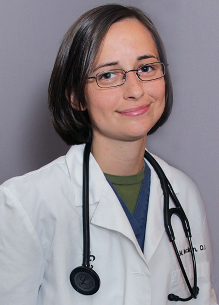 A woman with glasses wearing a white lab coat and a stethoscope smiles gently.