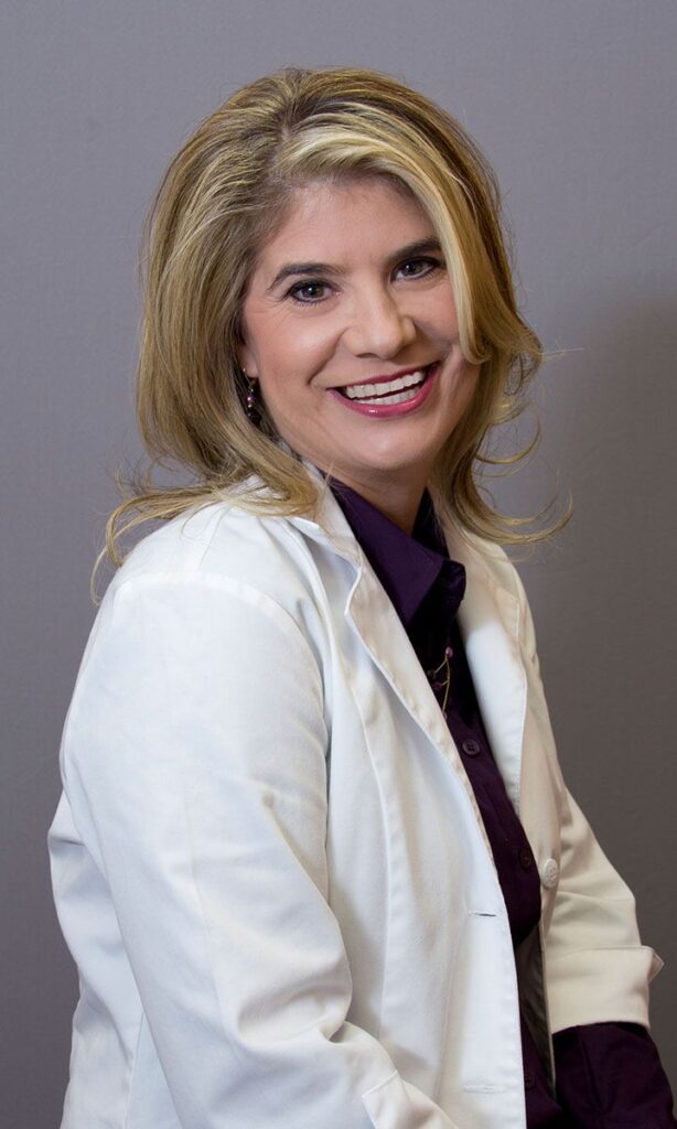 Smiling woman in a white lab coat over a purple blouse.