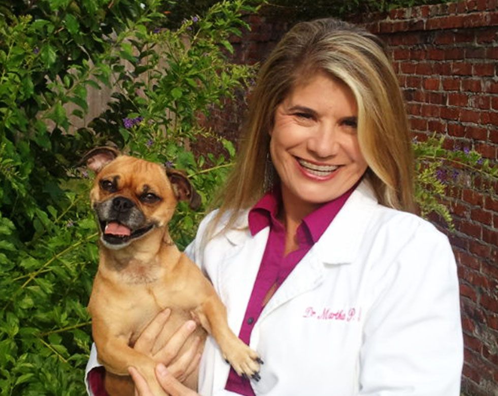 A smiling woman in a lab coat holding a small, happy dog.